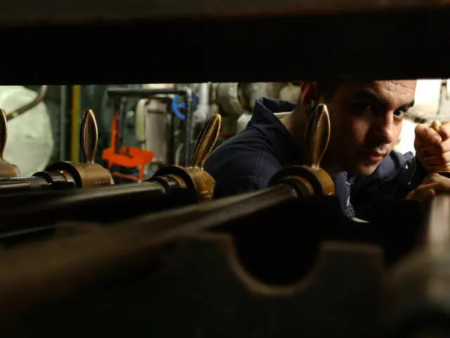 The image shows a man working on a machine in a factory, surrounded by various tools and equipment....