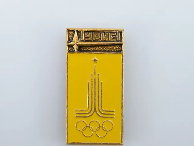 The image shows a yellow enamel pin with the Olympic logo on it, which is a badge of the USSR...