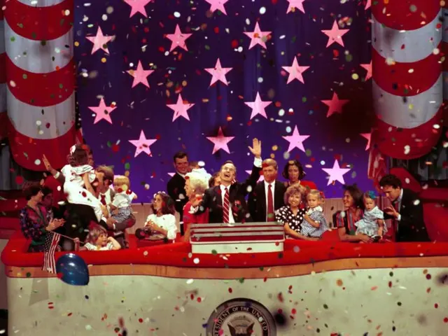 The image shows a group of people standing on top of a stage, with a podium in the center. There is...