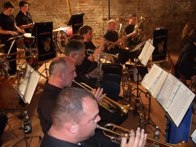 The image shows a group of men playing trumpets in a room with a brick wall in the background....