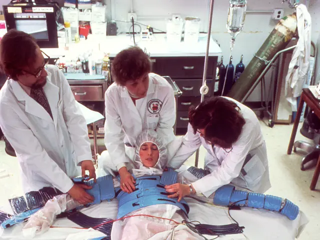 The image shows a group of four people in white lab coats working on a patient lying on a gurney in...