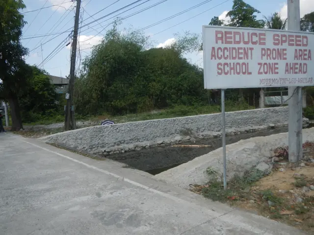 The image shows a road with a sign on the side that reads "Reduce Speed Accident Prone Area School...