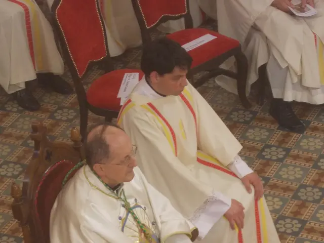The image shows a group of priests sitting in chairs in a church, with some of them holding papers...