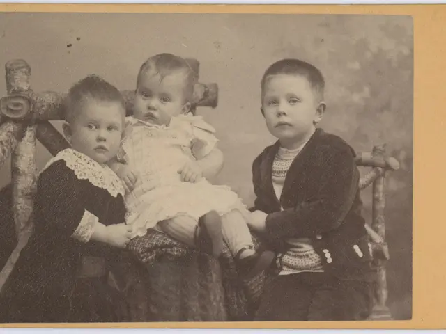 The image shows an old photo of three children sitting on a bench, with one of them holding a baby...
