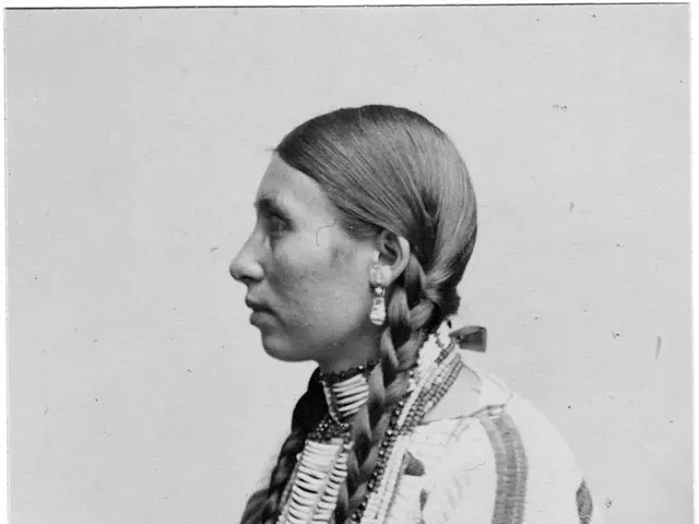 The image shows an old black and white photo of a Native American woman wearing traditional...