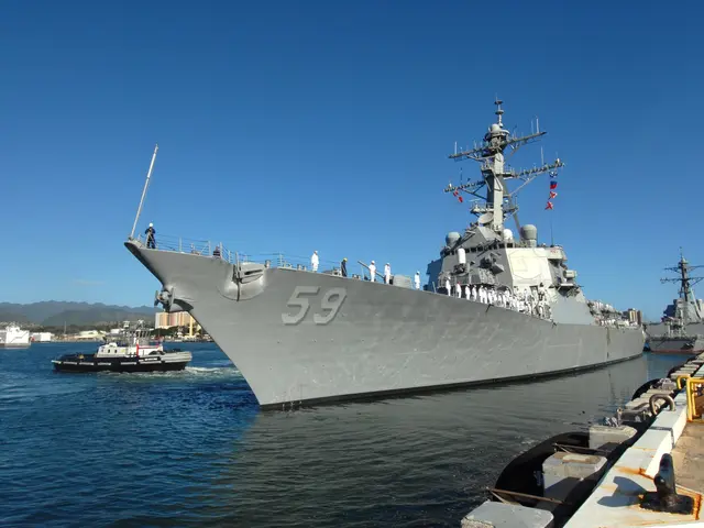 The image shows a navy ship docked in the water near a dock, with people on board. On the right...