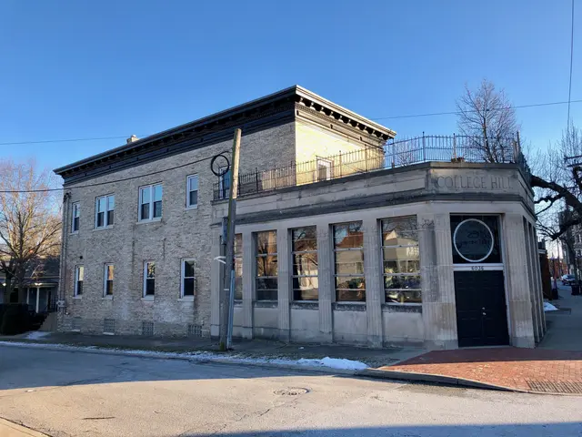The image shows an old building on the corner of a street, surrounded by trees, poles, wires, and...