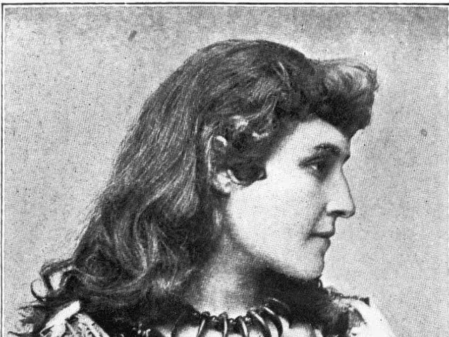 The image shows an old black and white photo of a woman with long hair wearing a dress. At the...