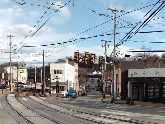 The image shows a yellow school bus driving down a street lined with tall buildings, electric poles...