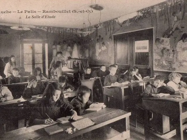 The image shows an old black and white photo of a classroom full of children sitting at desks, with...