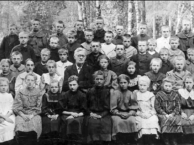 The image shows a black and white photo of a group of children posing for a picture in front of a...