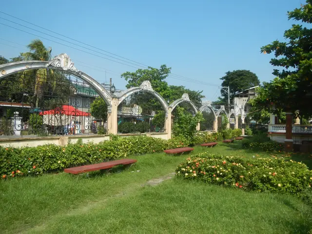 The image shows a park with lush green grass, vibrant flowers, and a variety of plants and trees....