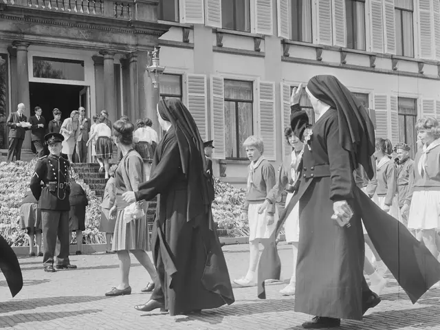 The image shows a group of nuns walking down a street in front of a building, with a few people...