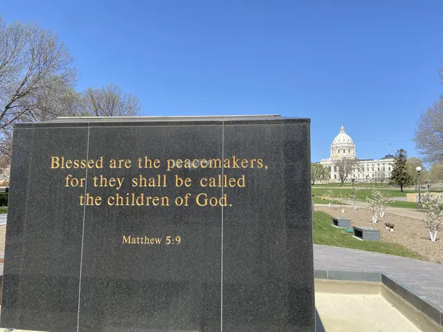 The image shows a memorial stone with the words "Blessed are the peacemakers, for they shall be...