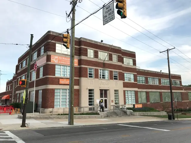 The image shows a large brick building on the corner of a street, surrounded by electric poles with...