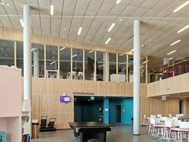 The image shows a large room filled with lots of tables and chairs, sofas, stools, bookshelves,...