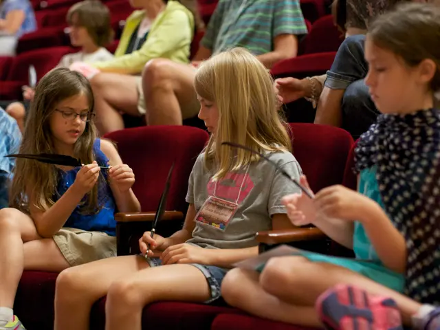 The image shows a group of young girls sitting in a theater, each holding a pair of scissors in...