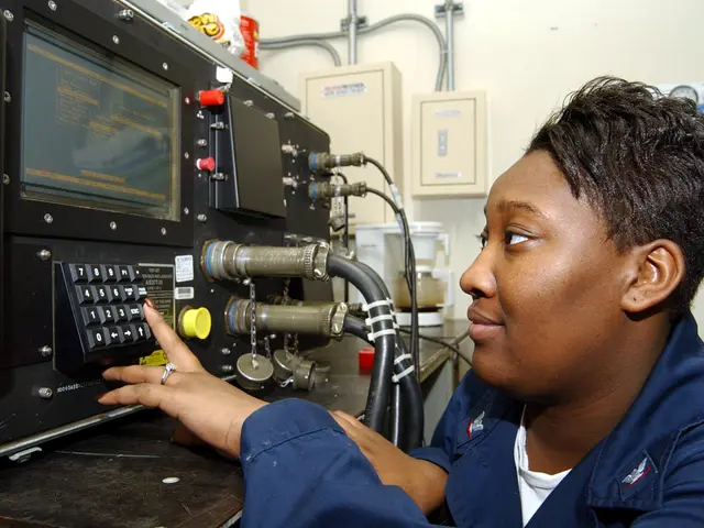 The image shows a woman in a blue uniform working on a machine in front of a wall with pipes and...