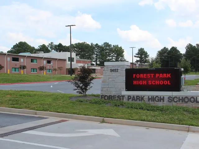 The image shows Forest Park High School, with a road in the foreground, grass on the ground, a wall...
