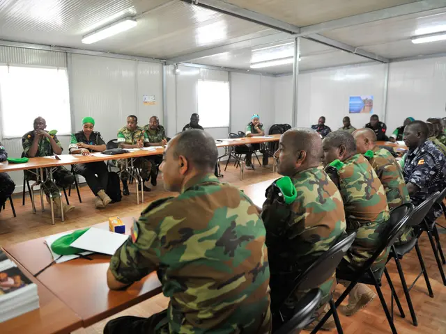The image shows a group of men in military uniforms sitting at tables in a room with books, papers,...