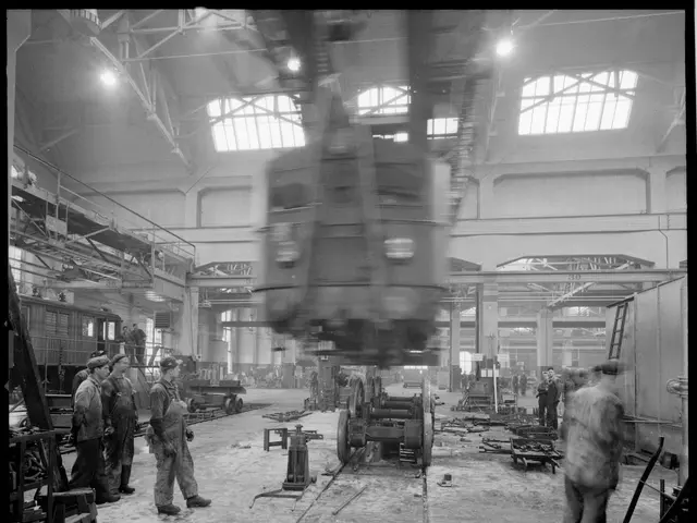 The image shows a black and white photo of a group of men working on a train in a factory. The men...