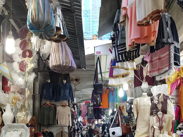 The image shows a bustling street market in the old city of Jerusalem, with a variety of items for...