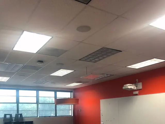 The image shows a classroom with tables and chairs arranged in it, a whiteboard on the wall, a...