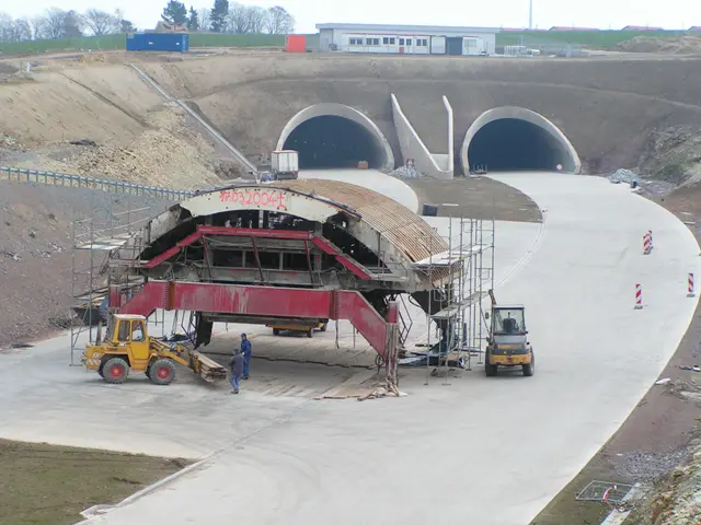 The image shows a construction site with a large tunnel in the middle of it. There are vehicles on...