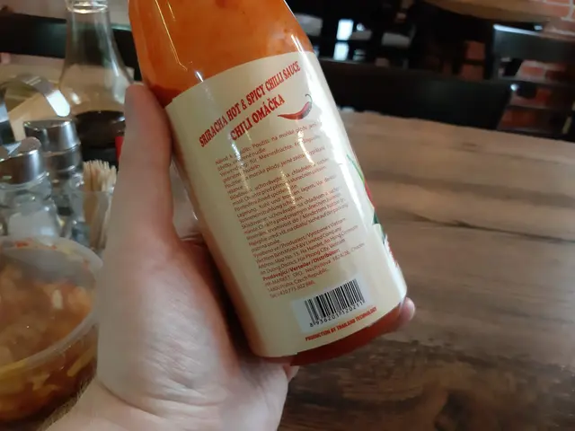 The image shows a person holding a bottle of sriracha hot and spicy chili sauce in their hand, with...