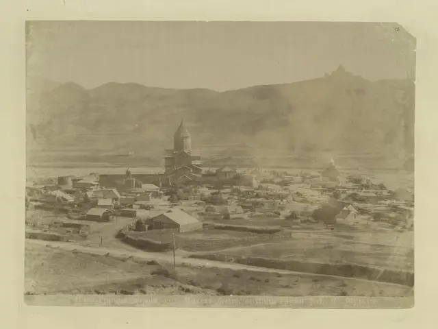 The image shows an old black and white photo of a small town with a church in the center,...