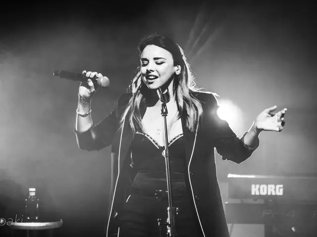 The image shows Demi Lovato performing at the O2 Academy Brixton in London. She is standing in...