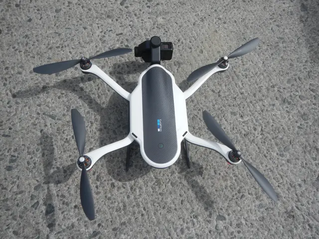 The image shows a white drone with four propellers and a camera on top of it, hovering on the...