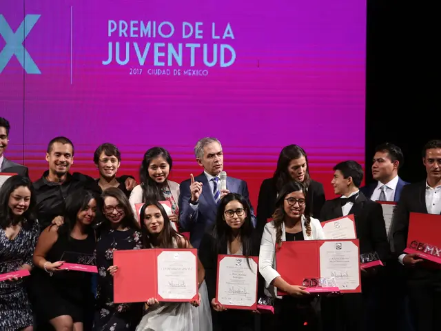 The image shows a group of people standing on top of a stage, smiling and holding certificates in...