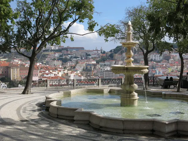 The image shows a fountain in the middle of a park with people sitting on benches around it. The...