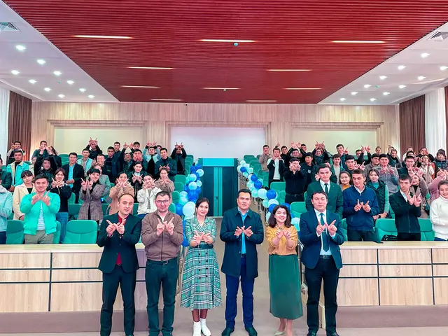 The image shows a group of people standing in front of a crowd of people, some of whom are clapping...