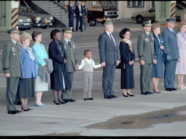 The image shows a group of people standing next to each other in military uniforms, with a man in...