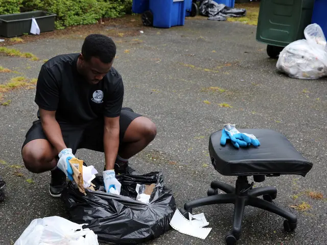 The image shows a man kneeling down next to a pile of trash, wearing a black t-shirt and blue...