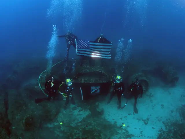 The image shows a group of scuba divers in the ocean with an American flag on top of a shipwreck....