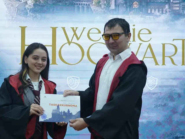 The image shows a man and woman standing side by side, both wearing graduation robes and holding a...