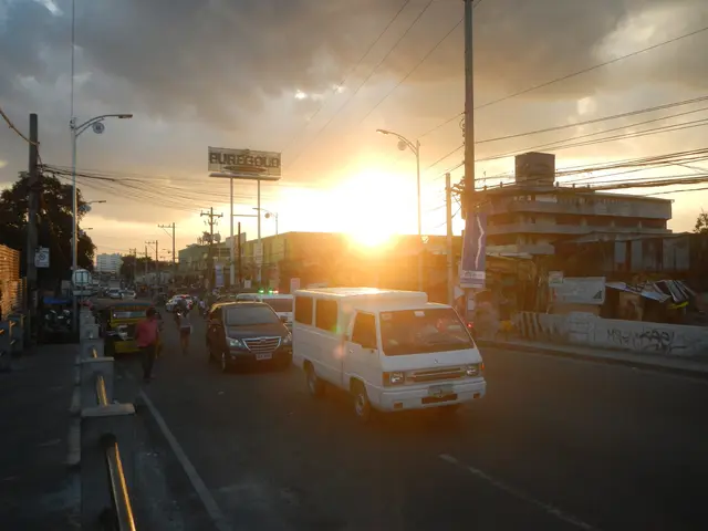 The image shows a van driving down a street lined with tall buildings, electric poles with wires,...