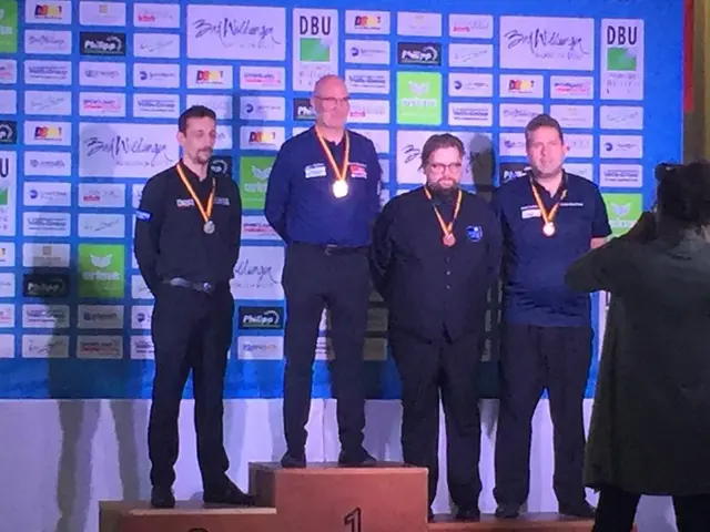 The image shows a group of five men standing on top of a podium, wearing medals around their necks....