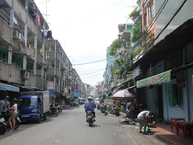 The image shows a bustling street in Hanoi, Vietnam, with people riding motorcycles and cars...