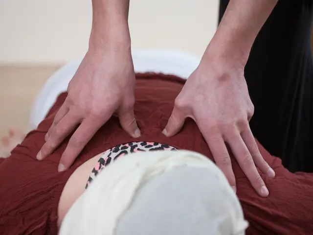 The image shows a woman receiving a back massage at a spa, with a wall in the background. She is...