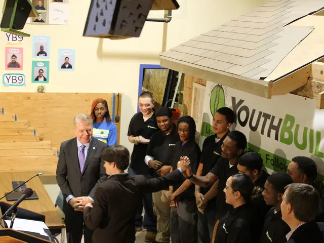 The image shows a group of people standing around a podium in front of a crowd. On the left side of...