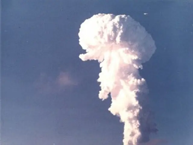 The image shows an atomic bomb exploding over the ocean, with a large plume of smoke billowing out...