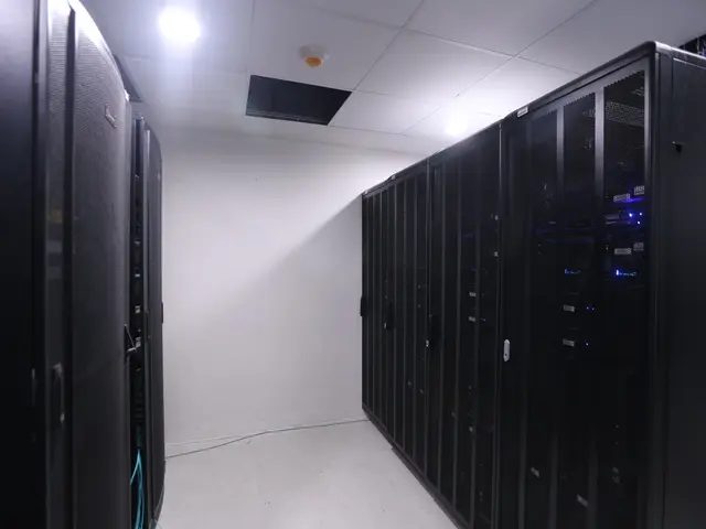 The image shows a row of servers in a data center, with a wall in the background and lights at the...